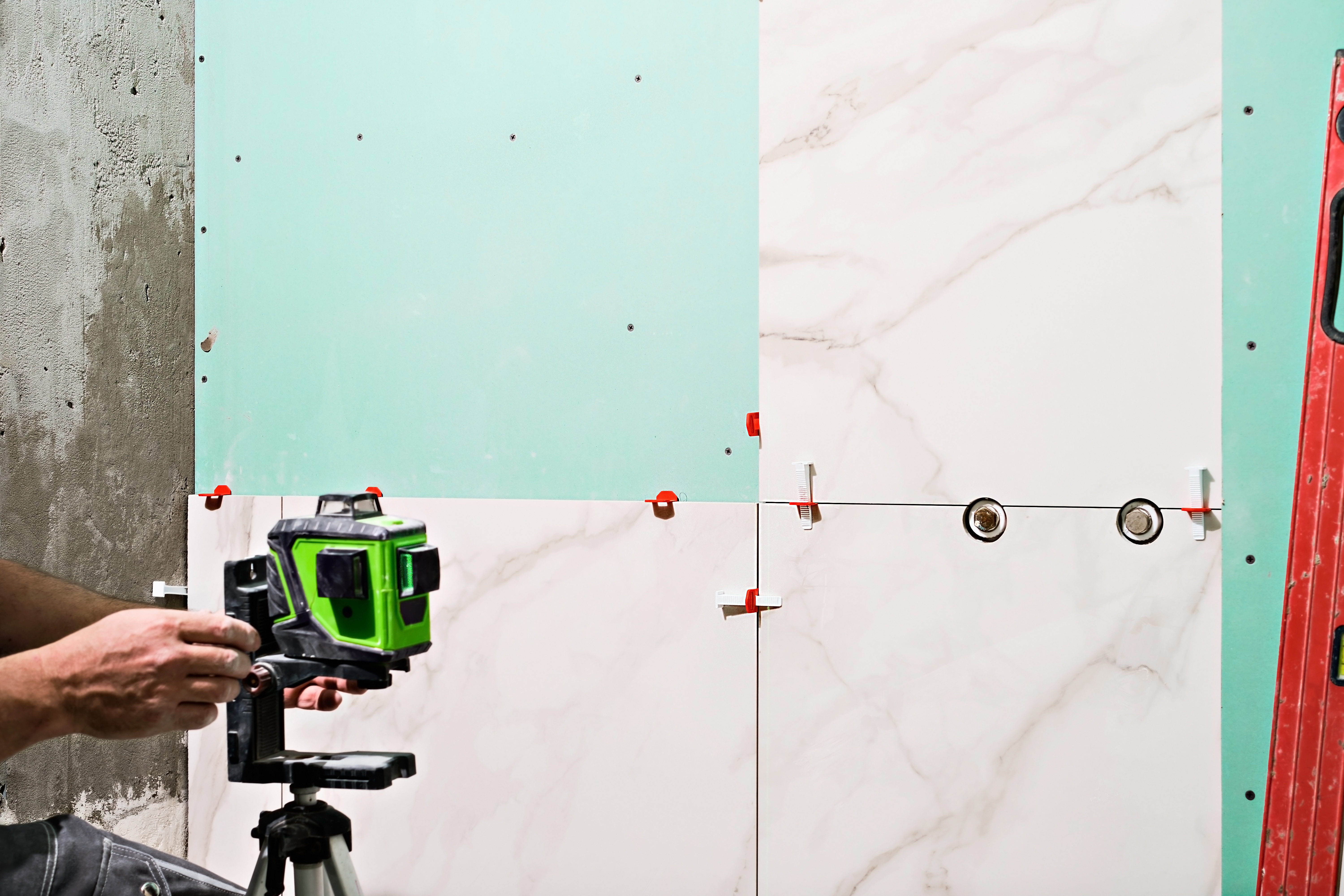 Laser metering during the renovation of the bathroom, the master adjusts the level. Construction tools and equipment tile sticker on the wall. Green lines of the laser beam for level measurement